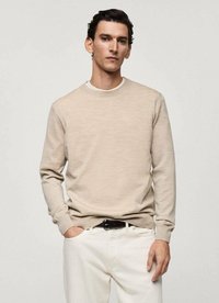 Maglione beige a girocollo realizzato in tessuto lavorato a maglia, con maniche lunghe e colletto a coste. Indossato con pantaloni bianchi e una cintura nera.