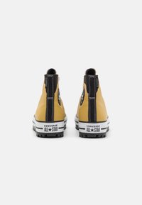 Žluté kožené vysoké tenisky s černými akcenty, gumovou podrážkou, bílými pruhy a vyraženým logem na patě. Texturovaný povrch a poutko.