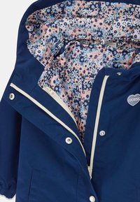 Marineblauwe jas met een bloemenpatroonvoering in roze, blauw en crème; voorzien van een ritssluiting, drukknoopsluiting en elastische manchet. 