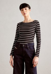 Schwarz-weißt gestreiftes Langarmhemd kombiniert mit dunkelblauen Jeans mit geradem Beinausschnitt und sichtbaren Nähten.