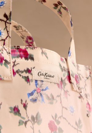 Cvetna torba za nošenje v mehki kremni barvi z rožnatimi in modrimi cvetovi, izdelana iz tkanine, z dvema ročajema. Na strani ima označbo blagovne znamke.