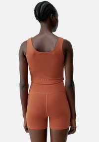 Atletisk kort topp och shorts set i bränd orange, med en åtsittande design, slät textur och minimal sömdetaljering på baksidan.