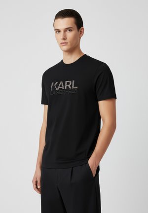 Musta t-paita, jossa etupuolella kohokuvioinen "KARL LAGERFELD" -logo. Pehmeä kangas, pyöreä pääntie, lyhyet hihat ja vartalonmyötäinen leikkaus.