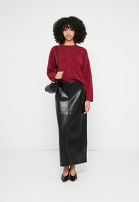 Burgundský sveter s textúrou a dlhými rukávmi, doplnený čiernou koženou maxi sukňou. Modelka nesie malú čiernu kabelku a má obuté čierne topánky.