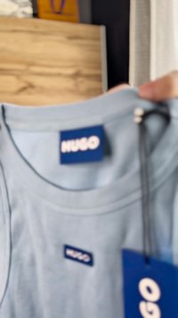 Himmelblaues Baumwoll-T-Shirt mit rundem Ausschnitt, ausgestattet mit einem weißen "HUGO"-Logo auf einem blauen Etikett und einem beiliegenden blauen Preisschild.