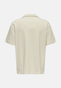 Polo majica kratkih rukava u svijetloj krem boji, izrađena od mekog, teksturiranog materijala. Ima klasičan ovratnik i opušteni kroj s ravnim rubom.