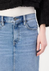 Jupe crayon en denim bleu clair avec une texture lisse, un design à cinq poches, une fermeture par bouton et des détails de dégradé subtils.