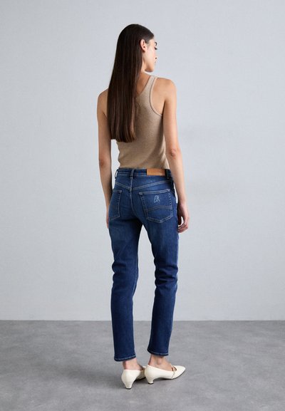 Λεπτά μπλε τζιν παντελόνια με πίσω τσέπες, καφέ φανέλα και κρεμ χρώματος ψηλοτάκουνες γόβες. Τα τζιν διαθέτουν δερμάτινη ετικέτα στη μέση.