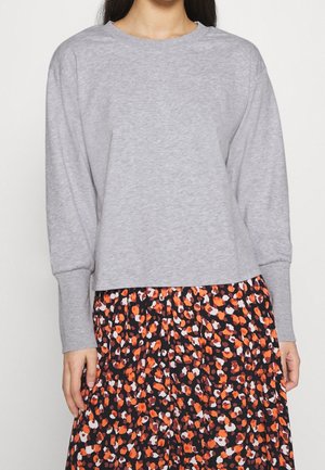 Grauer Pullover mit Rundhalsausschnitt und langen Ärmeln, kombiniert mit einem schwarzen Rock mit einem floralen Muster in Orange und Weiß.