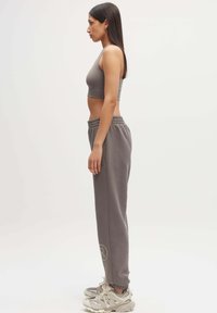 Grijze cropped tanktop gecombineerd met grijze sweatpants met een elastische tailleband. Draag met chunky beige sneakers. Zijaanzicht.