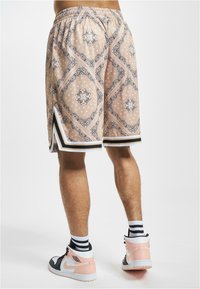 Shorts i en lys ferskenfarge med et mønster som har svarte detaljer, elastisk midje og hvit kanting ved hemmen.