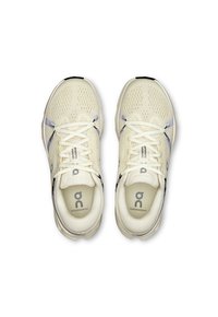 Chaussures de sport beiges en matériau en maille ; équipées d'une languette rembourrée, de lacets, d'accents réfléchissants et d'un logo sur la semelle et sur la semelle intérieure.