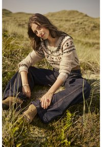 Bēša džemperis ar rakstainu yoku, platas zila denima bikses un brūni potīšu zābaki. Valkāts zālāja ārtelpās. Gludās tekstūras un brīva piegriezuma.