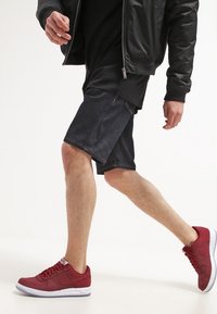 Tmavě modré džínové kraťasy se světlým prošitím, nošené s černou dlouhou košilí a červenými teniskami s bílou podrážkou. Ležérní, sportovní vzhled.