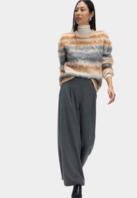 Weicher, mehrfarbiger Pullover mit gestreiften Mustern in Beige, Grau und Orange. Kombiniert mit hochtaillierter, grauer Hose mit weitem Bein.