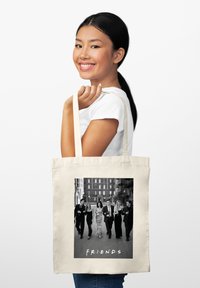 Bolsa de lona en color crema, que presenta una foto en blanco y negro de seis individuos con el texto "F.R.I.E.N.D.S." en la parte inferior.