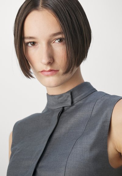 Gray sleeveless top with a high collar, featuring a subtle texture and streamlined design, accentuated by clean seams.