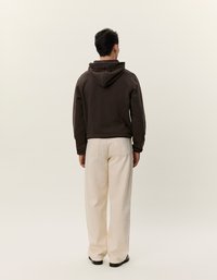 Felpa con cappuccio in cotone marrone scuro, abbinata a pantaloni larghi crema, mostrata di spalle. Design semplice, con dettagli minimi.