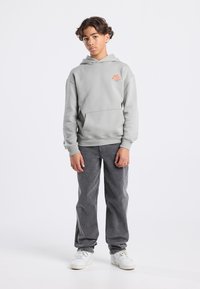 Gray hoodie with a front pocket and orange logo, paired with gray pants and white sneakers. Soft texture, relaxed fit, and minimalistic design.