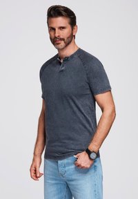 Krátký rukáv, tmavě šedý henley tričko s knoflíkovou légou a raglánovými rukávy, v kombinaci se světle modrými džíny.