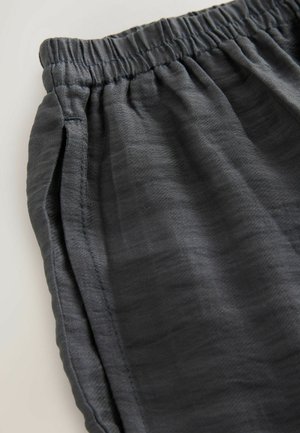 Pantalons gris à taille élastique en tissu léger et texturé, dotés de poches latérales et de détails de couture subtils.