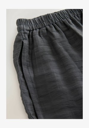 Pelēkas elastīgas jostas bikses, kas izgatavotas no viegla, teksturēta auduma, ar sānu kabatām un smalkiem izšuvuma elementiem.