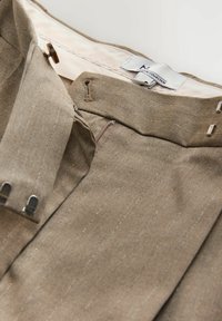 Pantalones de tela beige a rayas con cierre de cremallera y botón. Cuenta con pasadores para cinturón y acentos de hardware metálico. Interior forrado.
