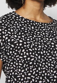 Czarna bluzka o gładkiej fakturze z rozsianym wzorem białych kropek, okrągłym dekoltem i krótkimi rękawami dla luźnego kroju.