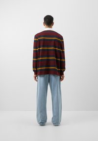 Bordeaux gestreifter Langarm-Oberteil mit mehrfarbigen Streifen; lockere Passform. Kombiniert mit hellblauen weit geschnittenen Jeans. Einfacher Halsausschnitt.