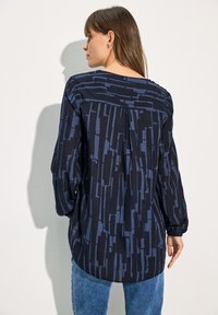 Langärmlige Bluse mit einem dunkelblauen Muster, die einen lässigen Schnitt, runden Halsausschnitt und leicht geraffte Rückendetails aufweist.