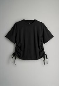 Fekete rövid ujjú póló összegyűrt oldalakkal, állítható megkötőkkel az alsó szélén és klasszikus kerek nyakkivágással. Puha, légáteresztő anyagból készült.