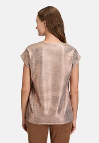 Haut rose doré métallisé à manches courtes avec texture à côtes horizontales et encolure ronde, associé à un pantalon marron.
