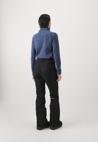 Pulič s visokom ovratnikom u plavoj boji s glatkom teksturom, uparen s crnim skijaškim hlačama koje imaju slim fit i detalj loga blizu članaka.