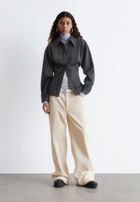 Gray button-up shirt with a collared neck over a lilac turtleneck. Beige wide-leg corduroy pants and chunky black shoes.