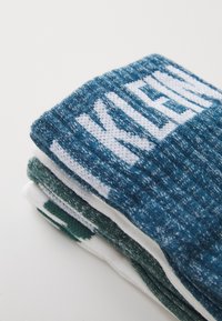 Paquete de calcetines en tonos verde azulado y blanco. Textura de punto con una mezcla de colores. Diseño de logo destacado en la parte superior de cada calcetín.