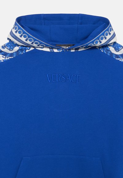 Plava dukserica s kapuljačom ukrašenom uzorkom, vezom 'VERSACE' logotipa i kengur džepom sprijeda, s glatkom teksturom.