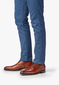 Bruine leren dress schoenen met een ronde neus, eenvoudig ontwerp, en blauwe slim-fit broek zichtbaar vanaf de enkels naar beneden.