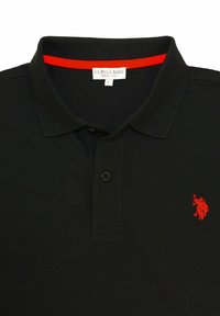 Černé polo tričko vyrobené z texturované tkaniny, s červeným podkladem límce a malým červeným logem hráče polo na levém prsu. Viditelný jeden knoflík.