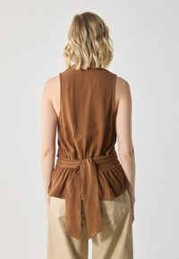Brauner ärmelloser Top mit tailliertem Oberteil und gerafftem Peplum-Saum, der mit einem passenden Stoffgürtel in der Taille gebunden ist. Glatte Textur.