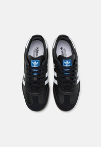 Zapatillas deportivas negras hechas de cuero y ante, con franjas blancas, una etiqueta de logo azul y una suela de goma texturizada.