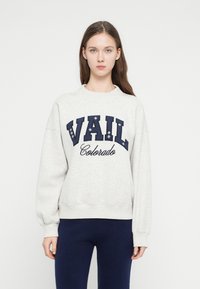 Hanorac gri deschis cu litere bleumarin inscripționate „VAIL Colorado.” Are guler rotund și manșete drepte plisate, cu o croială lejeră.