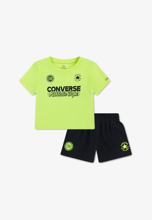 Neonsko zelena bombažna majica s črnim tiskom in logotipom "CONVERSE Athletic Dept."; kombinirana s črnimi kratkimi hlačami z ujemajočim logotipom in elastičnim pasom.