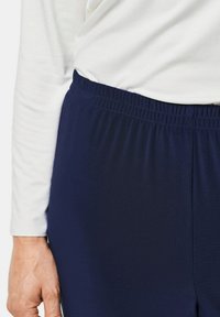 Marineblaue Hose mit elastischem Bund aus weichem Stoff, neben einem weißen Langarmoberteil präsentiert. Glatte Textur mit lässiger Passform.