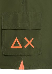 Giacca in tessuto verde oliva con una grande tasca frontale, decorata con simboli geometrici arancioni: un triangolo e una forma a "X".