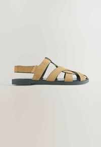 Sandale plate en daim couleur tabac avec bout ouvert, plusieurs brides croisées, semelle noire, et bride arrière ajustable avec fermeture Velcro.