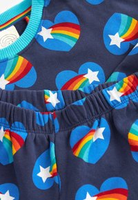 Katedra medvilninė apranga su tamsiai mėlynu fonu, papuoštu vaivorykštės širdelėmis ir baltomis žvaigždėmis. Jumpsuit'ai turi elastingą juosmenį. Ryškių spalvų įgulos iškirptė.