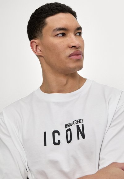Valge puuvillane T-särk, mille ees on must trükitud tekst "DSQUARED2 ICON", lühikesed varrukad ja klassikaline ümar kaelus.