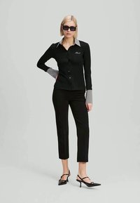 Camisa preta de botão com colarinho e punhos cinzentos, combinada com calças justas pretas e sandálias de salto pretas. O conjunto apresenta um design elegante e moderno.