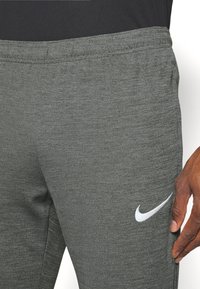 Pantalones deportivos grises hechos de una tela texturizada, con una cinturilla elástica y un logo blanco de Nike en el lado izquierdo.