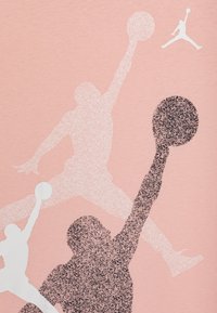  camiseta de color rosa claro con siluetas gráficas de jugadores de baloncesto en blanco y negro, con un logo de Jumpman en blanco.